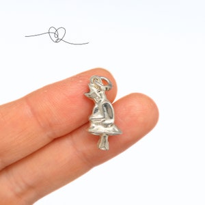 May include: Silver charm in the shape of a witch wearing a pointed hat and holding a broom.
