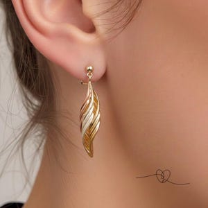 May include: A drop earring featuring a multi-toned metal design with swirling, elongated leaf-like segments in yellow, rose, and white gold tones. The earring is attached to a small, round stud post and hangs vertically from the earlobe.