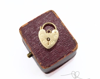 May include: A gold heart-shaped padlock with a keyhole in a burgundy velvet box.