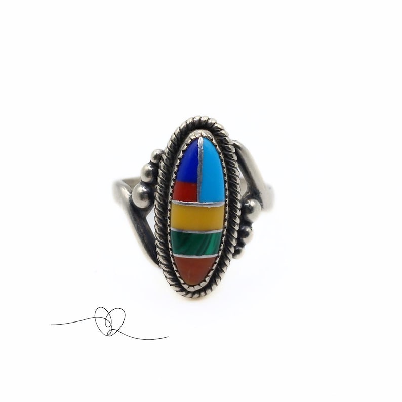 K&ouml;nnte beinhalten: Ein silberner Ring mit einem ovalen Stein, der in der Mitte eingesetzt ist. Der Stein besteht aus mehreren Farben von Einlegearbeiten, darunter Rot, Orange, Gelb, Gr&uuml;n, Blau und T&uuml;rkis.