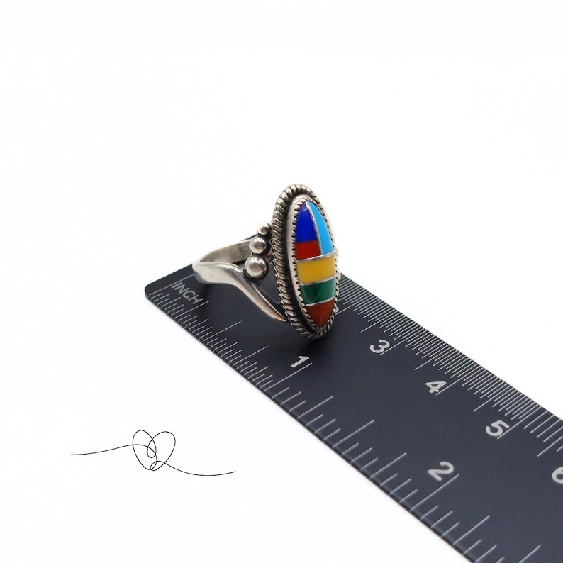 K&ouml;nnte beinhalten: Ein silberner Ring mit einem mehrfarbigen ovalen Stein, der in der Mitte eingesetzt ist. Der Stein besteht aus T&uuml;rkis, Rot, Gelb, Gr&uuml;n und Blau. Der Ring wird an einem Lineal gemessen und zeigt, dass er etwas mehr als 2,5 cm im Durchmesser hat.