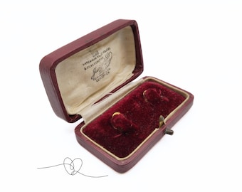 May include: An open red velvet jewelry box with a white interior. The box has a gold latch and is lined with red velvet. The box is labeled "WATCHMAKERS & JEWELLERS, J.H.UNIVERSITY, GLOUCESTER."