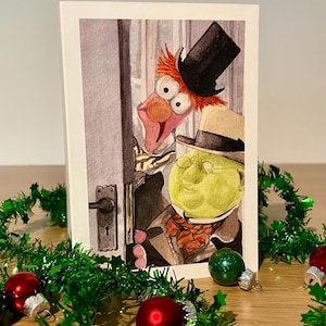 May include: A Christmas card with a watercolour illustration of two Muppet characters peeking through a doorway. The card is surrounded by green tinsel and red and green Christmas baubles. The Muppets are dressed in formal attire.