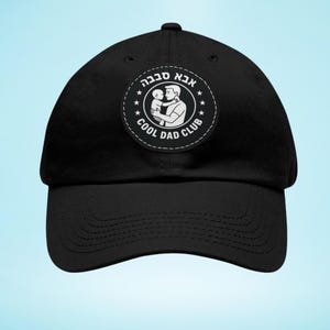 Puede incluir: Gorra de béisbol negra con visera curva. La gorra presenta un parche circular con el texto "Cool Dad Club" y una ilustración de un padre sosteniendo a un niño. El texto está en inglés y hebreo.