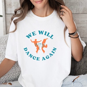 May include: White t-shirt with a blue circle graphic that says "We Will Dance Again" with two orange silhouettes of people dancing inside the circle.
