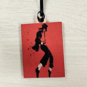 May include: A red rectangular wooden tag with a black silhouette of a person dancing on a red background. The tag has a black ribbon attached to it.