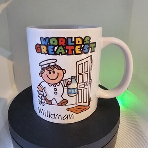 May include: White ceramic mug with a cartoon illustration of a milkman delivering milk. The mug has the text "WORLD'S GREATEST" in colorful letters and "Milkman" at the bottom.