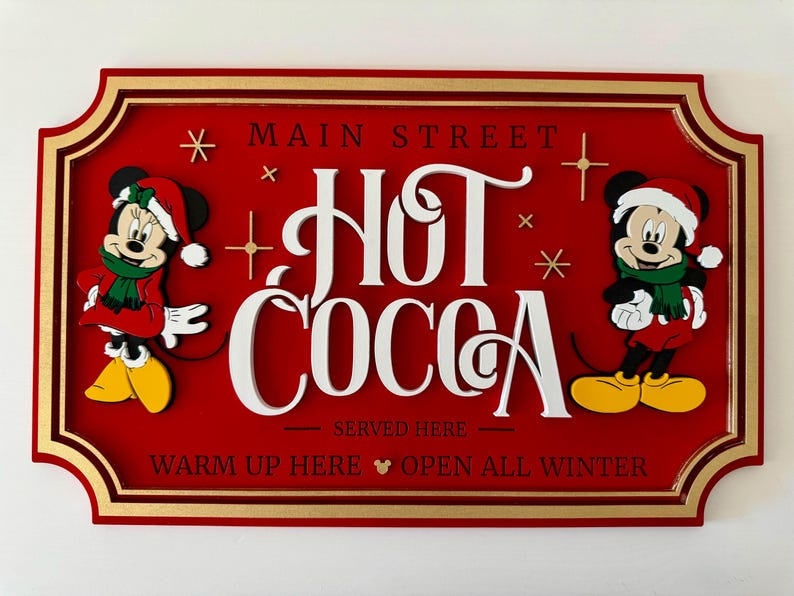 K&ouml;nnte beinhalten: Ein rotes Holzschild mit goldenem Rahmen, auf dem Mickey und Minnie Mouse in Weihnachtskleidung zu sehen sind. Das Schild lautet "Main Street Hot Cocoa Served Here Warm Up Here Open All Winter".