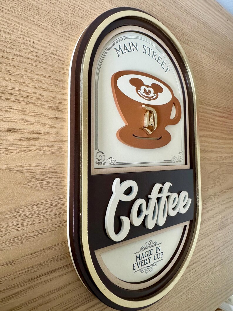 May include: A brown and gold oval sign with the text "Main Street Coffee" and a cartoon image of Mickey Mouse in a coffee cup. The sign also says "Magic in Every Cup".