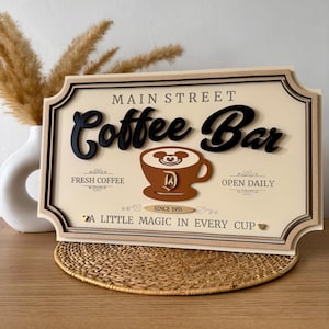 May include: A wooden sign with the text "Main Street Coffee Bar" in black lettering. The sign features a brown coffee cup with Mickey Mouse ears and a gold Disney "D" logo. The sign also includes the text "Fresh Coffee", "Open Daily", "Since 1955", and "A Little Magic in Every Cup".