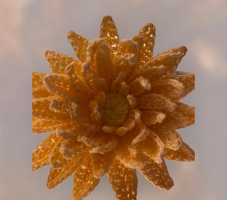 May include: A handmade, crocheted flower in shades of yellow and gold. The flower features multiple layers of petals with a detailed, openwork design. The centre of the flower is a lighter yellow, creating contrast. The overall effect is a textured, three-dimensional floral design.