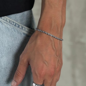 Könnte beinhalten: Ein silbernes Seilkettenarmband, das an einem Handgelenk getragen wird. Das Armband ist schlicht und elegant und wäre ein tolles Geschenk für jeden Anlass.