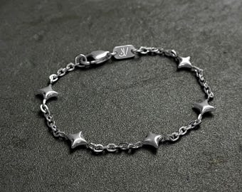 May include: A silver chain bracelet with a series of small, star-shaped charms. The bracelet has a clasp closure.