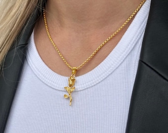 Può includere: Una collana con catena dorata con un ciondolo a forma di rosa. La rosa è dettagliata e ha uno stelo e foglie.