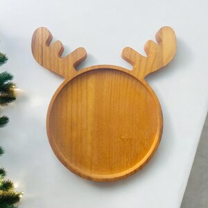 May include: A wooden serving tray shaped like a reindeer with a round centre and antlers. The tray is made of light brown wood and is perfect for serving snacks or appetizers.
