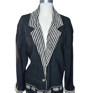 May include: Black blazer with white striped lapels and cuffs. The blazer features a decorative elephant pattern along the bottom edge and on the pockets. The blazer has two gold-colored buttons.