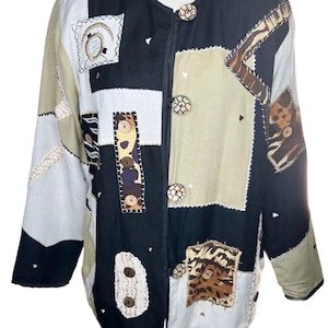 May include: A long-sleeve jacket featuring a patchwork design in black, beige, and white. The garment includes various textured fabric squares, animal print accents, and four round, patterned buttons down the front closure.