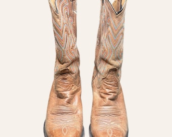 May include: A pair of tan leather cowboy boots featuring a pointed toe and a tall shaft. The upper portion of the boots is decorated with intricate, multi-coloured stitching in shades of blue, orange, and yellow, creating a wave-like pattern.