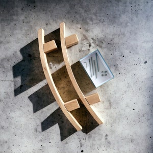 May include: Wooden curved shelf components with hardware. Two curved wooden pieces with rectangular supports are positioned on a concrete surface. A small box contains screws and other hardware, suggesting assembly is required.