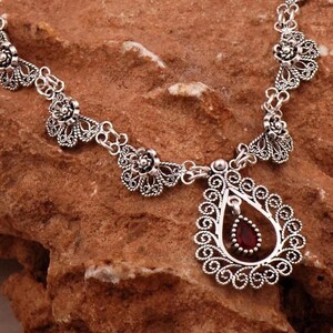 May include: A silver necklace with a delicate filigree design and a teardrop-shaped pendant with a red gemstone.