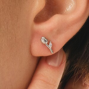 A pair of small silver earrings featuring a minimalist tulip shape adorned with sparkling white zircon stones, rhodium‑plated for a bright finish.