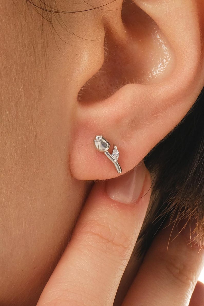 A pair of small silver earrings featuring a minimalist tulip shape adorned with sparkling white zircon stones, rhodium‑plated for a bright finish.