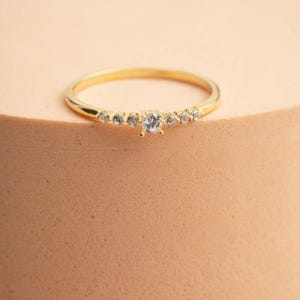 A close‑up of a thin silver ring with green gold plating and sparkling zircon stones, featuring a larger 2.5 mm center stone and smaller 1.5 mm accents.