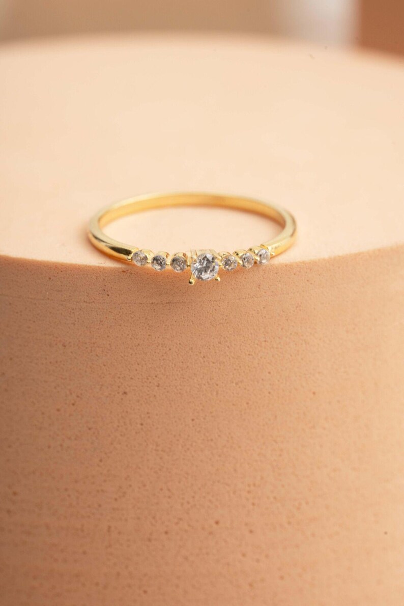 A close‑up of a thin silver ring with green gold plating and sparkling zircon stones, featuring a larger 2.5 mm center stone and smaller 1.5 mm accents.