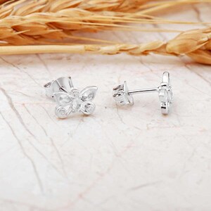 Mini butterfly earrings made of rhodium‑plated sterling silver with a white zircon stone, measuring 6 mm by 9 mm.