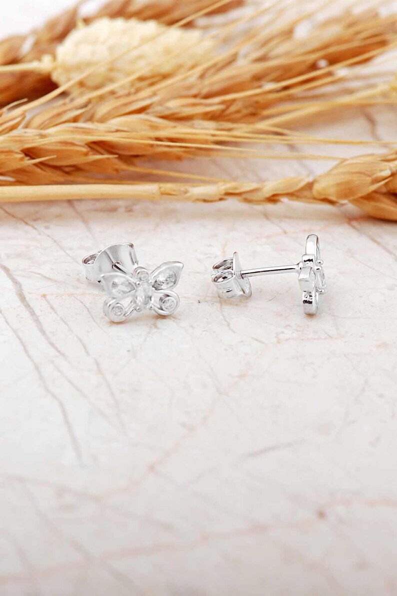Mini butterfly earrings made of rhodium‑plated sterling silver with a white zircon stone, measuring 6 mm by 9 mm.