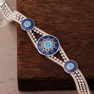 A handcrafted 925 sterling silver woven mesh bracelet featuring a round central plate with the intricate Sun of Mardin motif filled with colorful enamel.