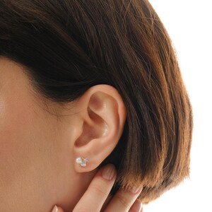 A pair of mini 925 sterling silver stud earrings featuring a detailed seashell and starfish motif accented with a small white pearl and butterfly backs.