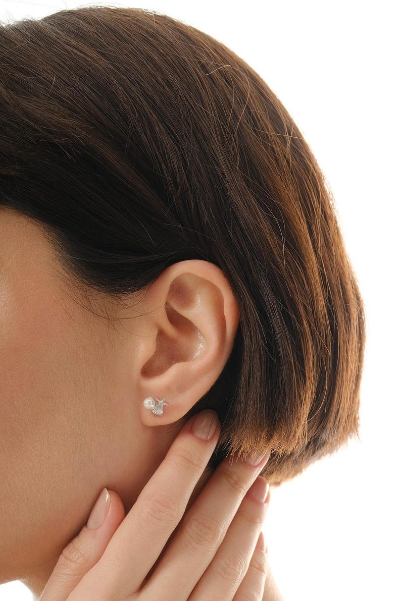 A pair of mini 925 sterling silver stud earrings featuring a detailed seashell and starfish motif accented with a small white pearl and butterfly backs.