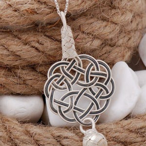 May include: A silver necklace with a detailed, intricate knot pendant. The pendant is made of woven silver wire and has a small, round silver bead at the bottom.