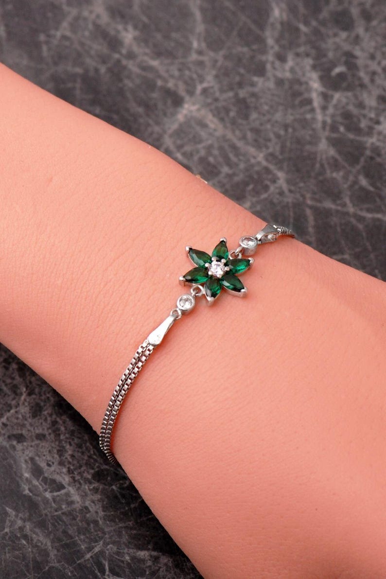 A delicate 925 sterling silver bracelet featuring a centrally placed lotus flower motif set with a brilliant gemstone, attached to a fine chain with an extension link.