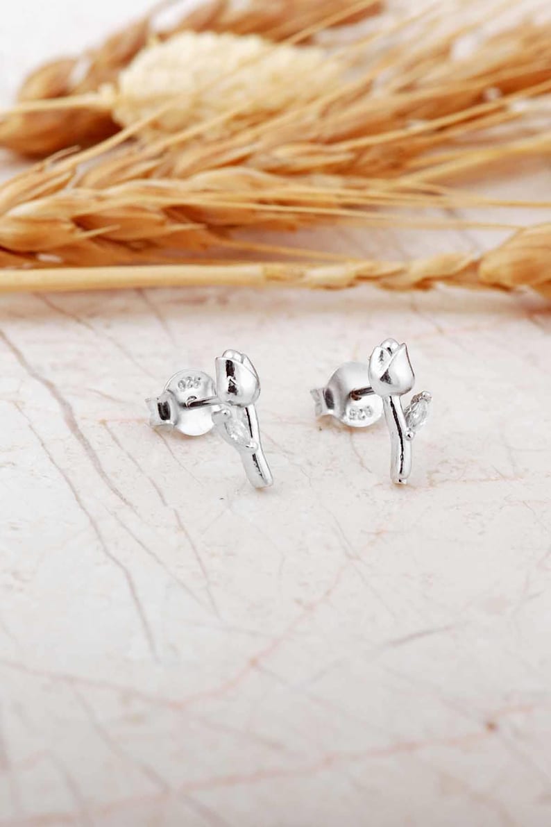 A pair of small silver earrings featuring a minimalist tulip shape adorned with sparkling white zircon stones, rhodium‑plated for a bright finish.