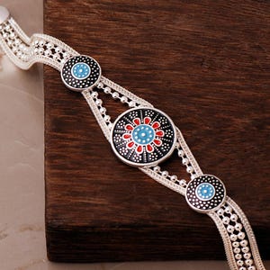 A handcrafted 925 sterling silver woven mesh bracelet featuring a round central plate with the intricate Sun of Mardin motif filled with colorful enamel.