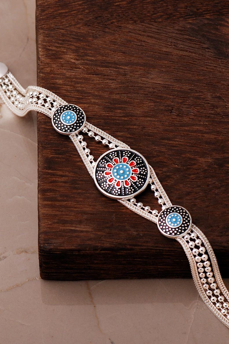A handcrafted 925 sterling silver woven mesh bracelet featuring a round central plate with the intricate Sun of Mardin motif filled with colorful enamel.
