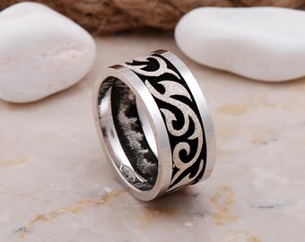 May include: A wide silver-toned ring featuring a prominent black inlay band that wraps around the exterior. The black inlay is decorated with a continuous, raised silver-toned swirling pattern that creates a distinct contrast against the dark background.