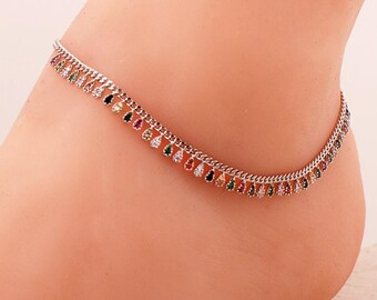 May include: A silver-toned metal anklet chain featuring a series of small, dangling, teardrop-shaped charms. Each charm is encrusted with a tiny, multi-coloured gemstone, including shades of red, green, blue, yellow, and clear white crystals.