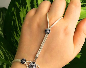Puede incluir: Una pulsera de mano de plata con un diseño de cadena tejida delicada. La pieza incluye cuatro adornos circulares con centros azul oscuro y patrones florales plateados intrincados, que conectan la pulsera con una presilla para el dedo.