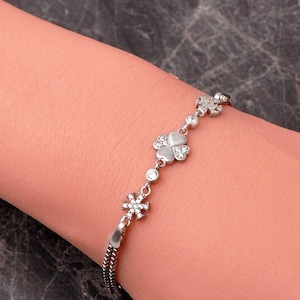 A delicate 925 sterling silver box chain bracelet featuring a four-leaf clover and snowflake charm set with clear cubic zirconia stones.