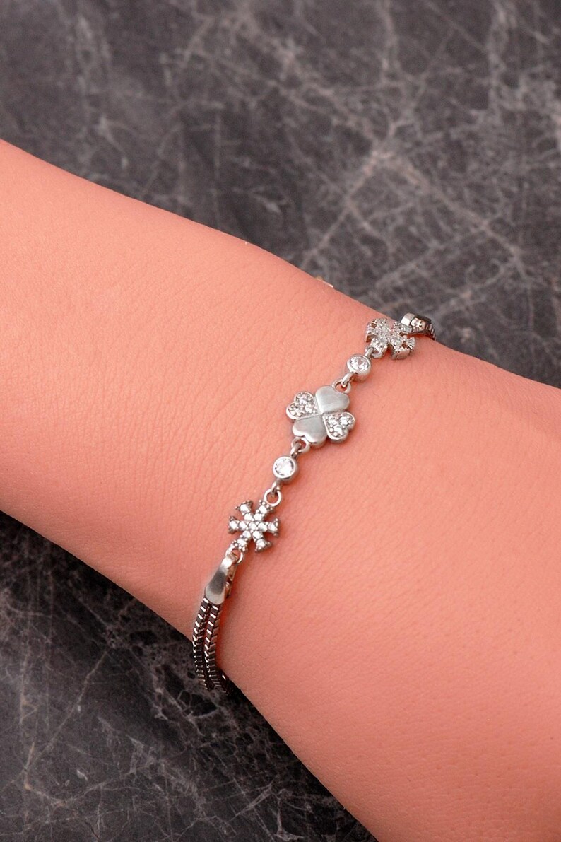 A delicate 925 sterling silver box chain bracelet featuring a four-leaf clover and snowflake charm set with clear cubic zirconia stones.
