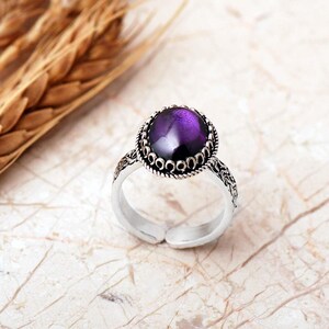 Adjustable oval ring made of 925 sterling silver with a green peridot stone on one side and a purple amethyst stone on the other, showing an oxidized antique finish.