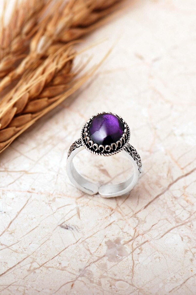 Adjustable oval ring made of 925 sterling silver with a green peridot stone on one side and a purple amethyst stone on the other, showing an oxidized antique finish.