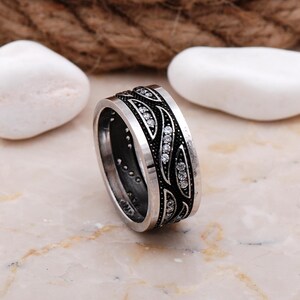 Handmade 925 sterling silver women's 9 mm wide wedding band adorned with sparkling cubic zirconia stones and finished in shiny white rhodium plating.