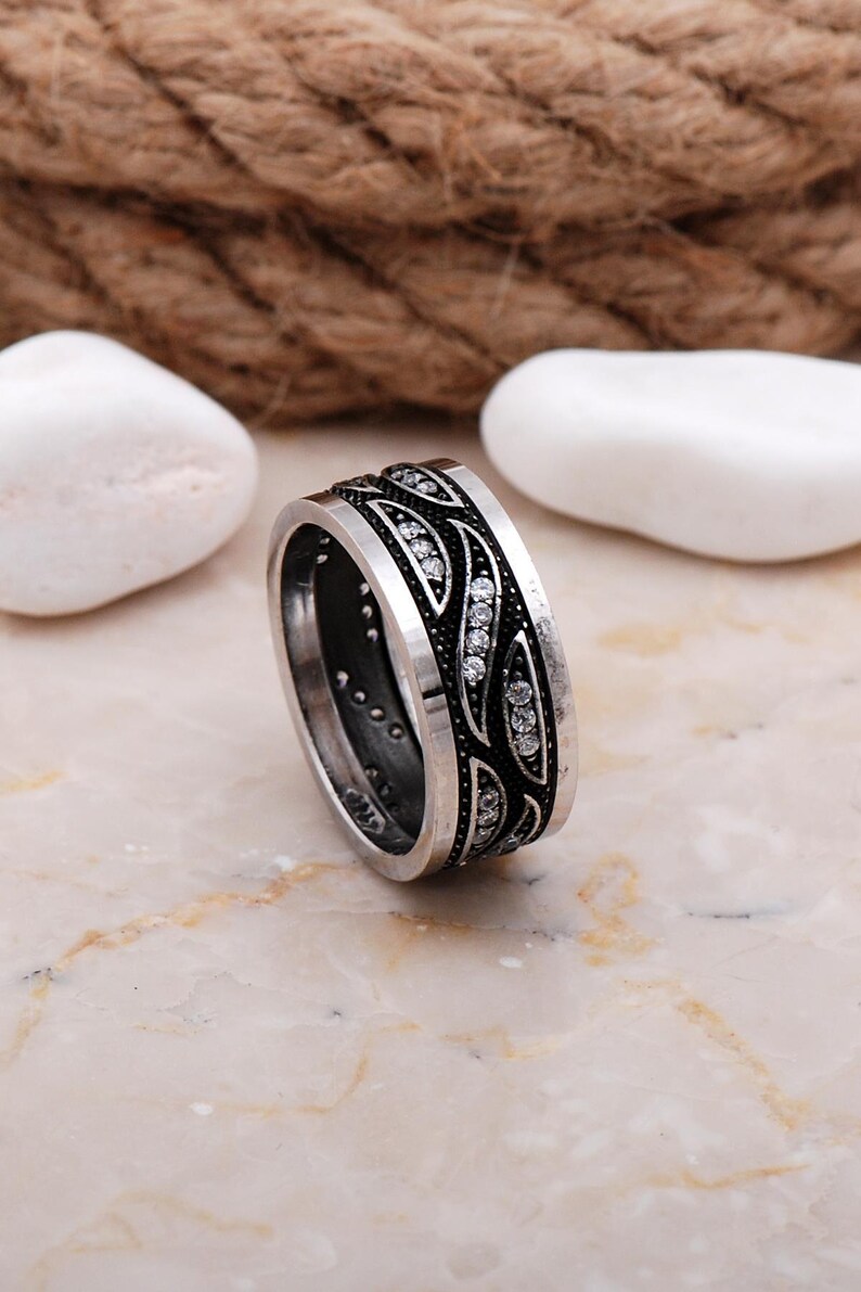 Handmade 925 sterling silver women's 9 mm wide wedding band adorned with sparkling cubic zirconia stones and finished in shiny white rhodium plating.