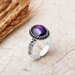 Adjustable oval ring made of 925 sterling silver with a green peridot stone on one side and a purple amethyst stone on the other, showing an oxidized antique finish.