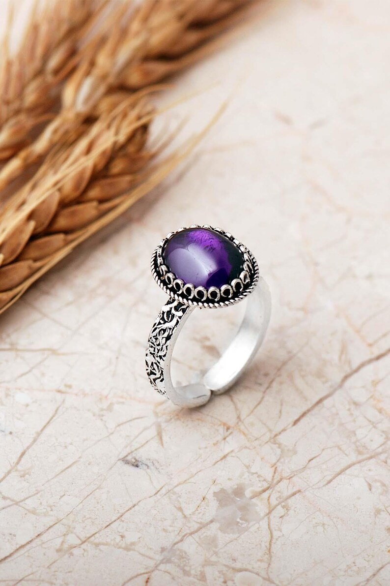 Adjustable oval ring made of 925 sterling silver with a green peridot stone on one side and a purple amethyst stone on the other, showing an oxidized antique finish.