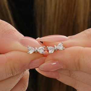 Mini bow‑shaped earrings made of rhodium‑plated sterling silver with a single white zircon stone on each side, measuring 4 mm tall by 1 cm wide.
